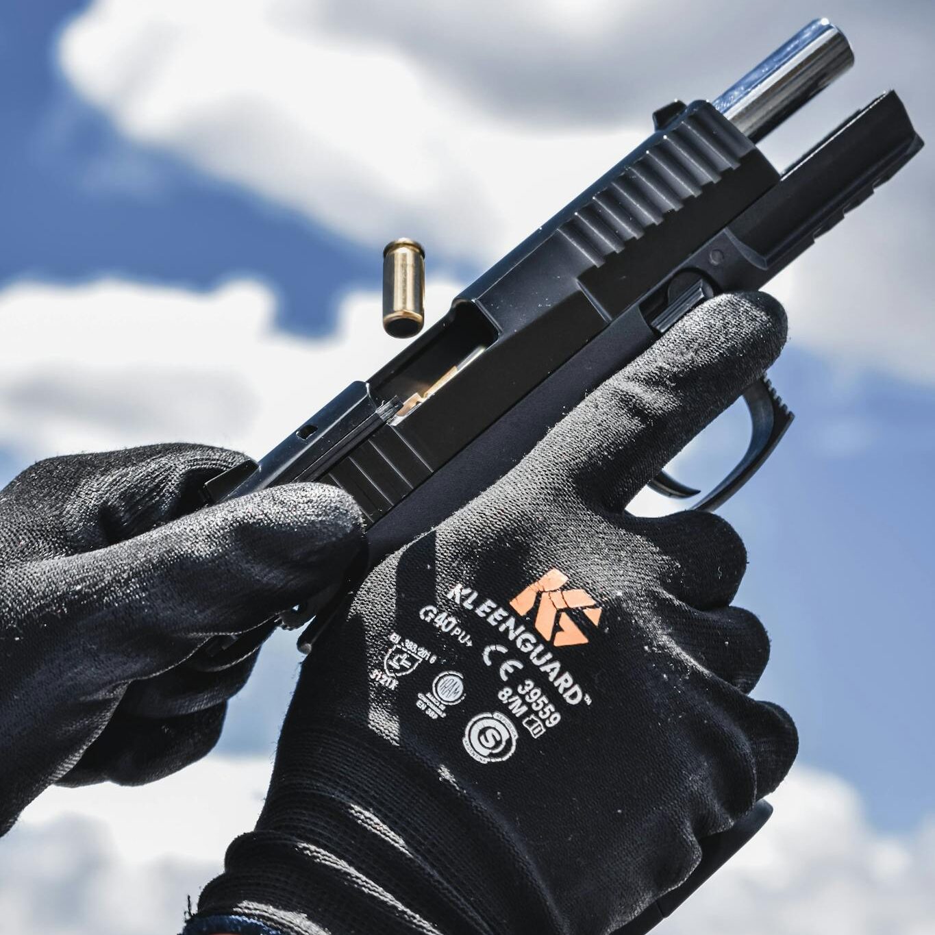 Detailed image of gloved hands reloading a pistol against a bright sky background.